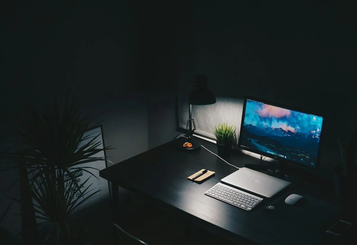 Bureau compact sombre avec un seul écran, une lampe et peu d’accessoires