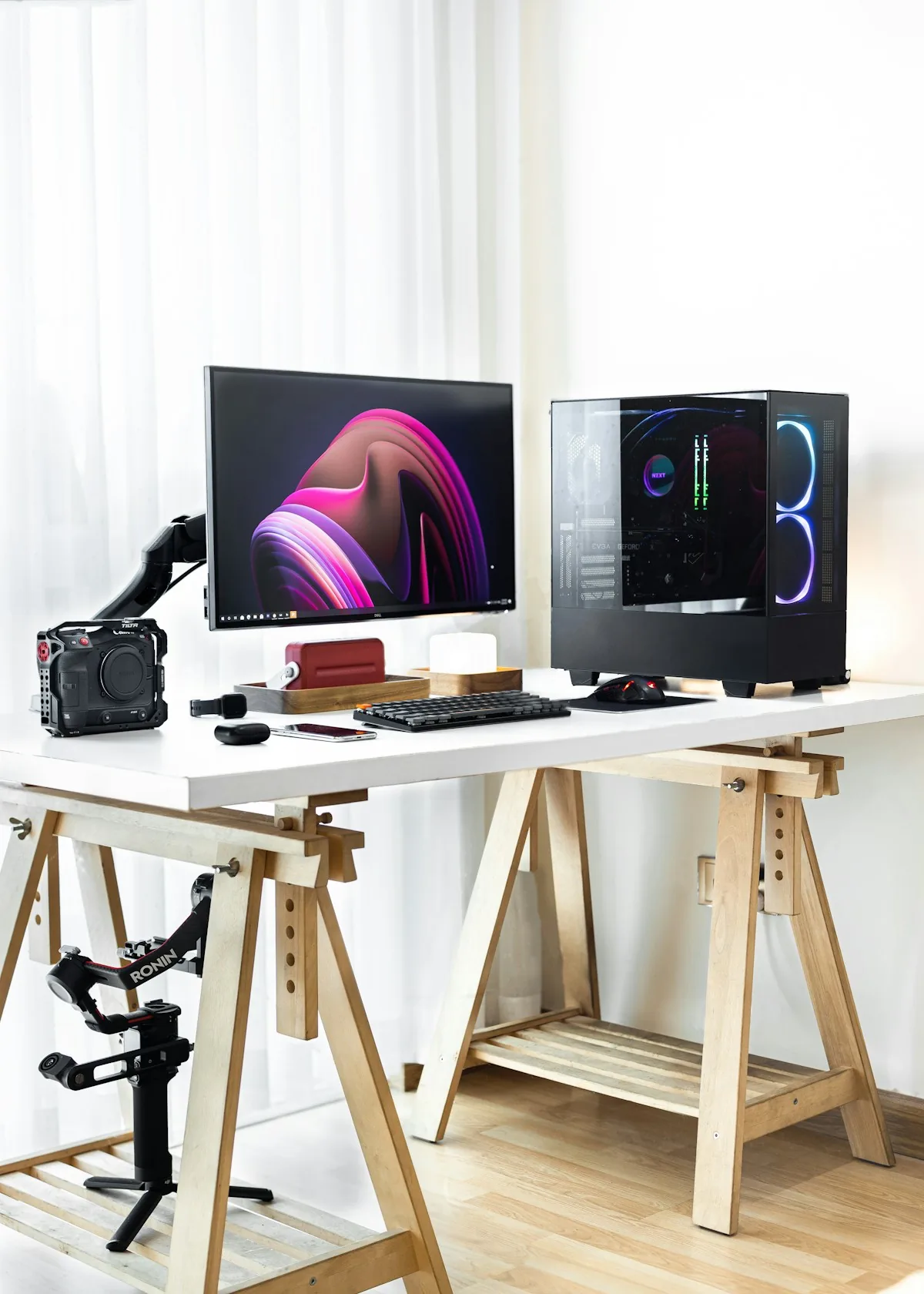 Bureau blanc sur tréteaux en bois avec un écran, un PC vitré et une lumière naturelle