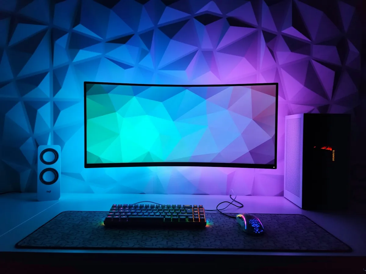 Setup gaming avec écran incurvé, bureau et mur géométrique éclairés en bleu et violet